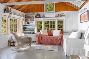 Ein gemütliches Zimmer mit Fernseher, Schaukelstuhl, Sofa und Bücherregal.
