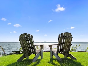 Zwei Adirondack-Stühle mit Blick auf einen See, bewölkter Himmel.