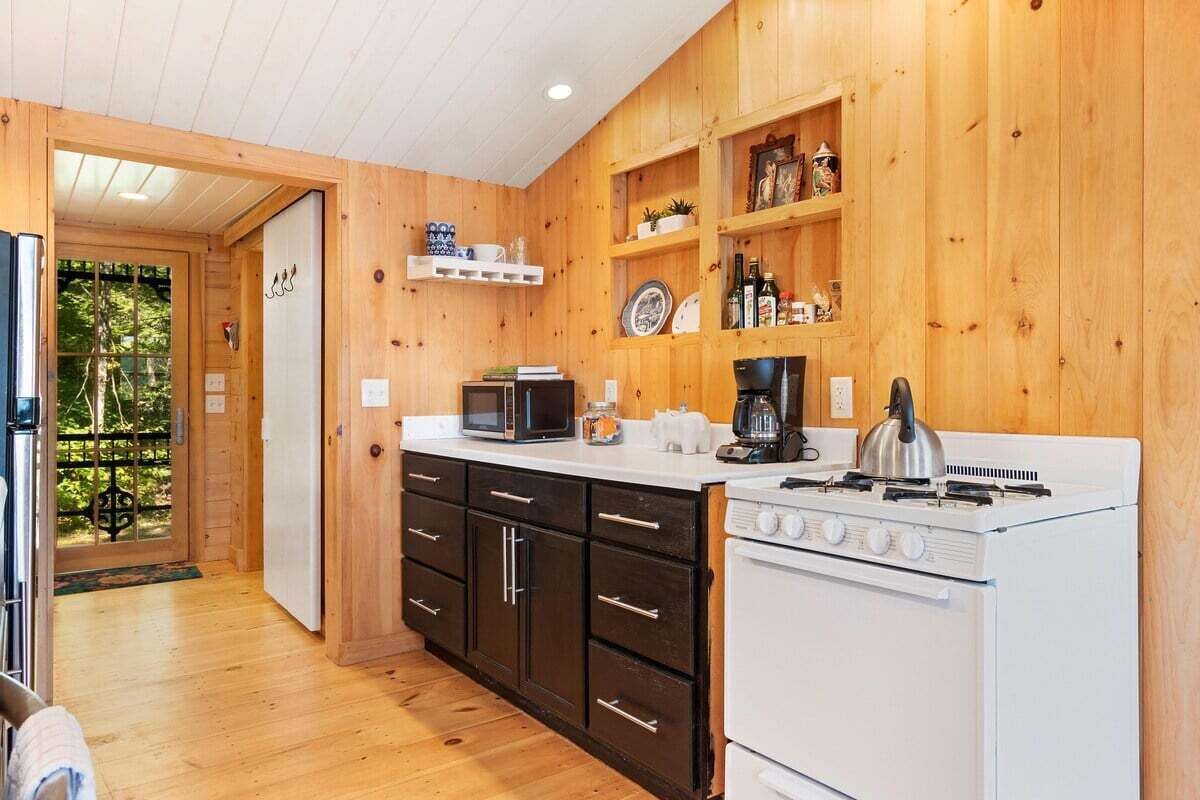 Cocina compacta con paredes de madera, estufa blanca, gabinetes negros y un microondas.
