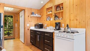 Cocina compacta con paredes de madera, estufa blanca, gabinetes negros y un microondas.