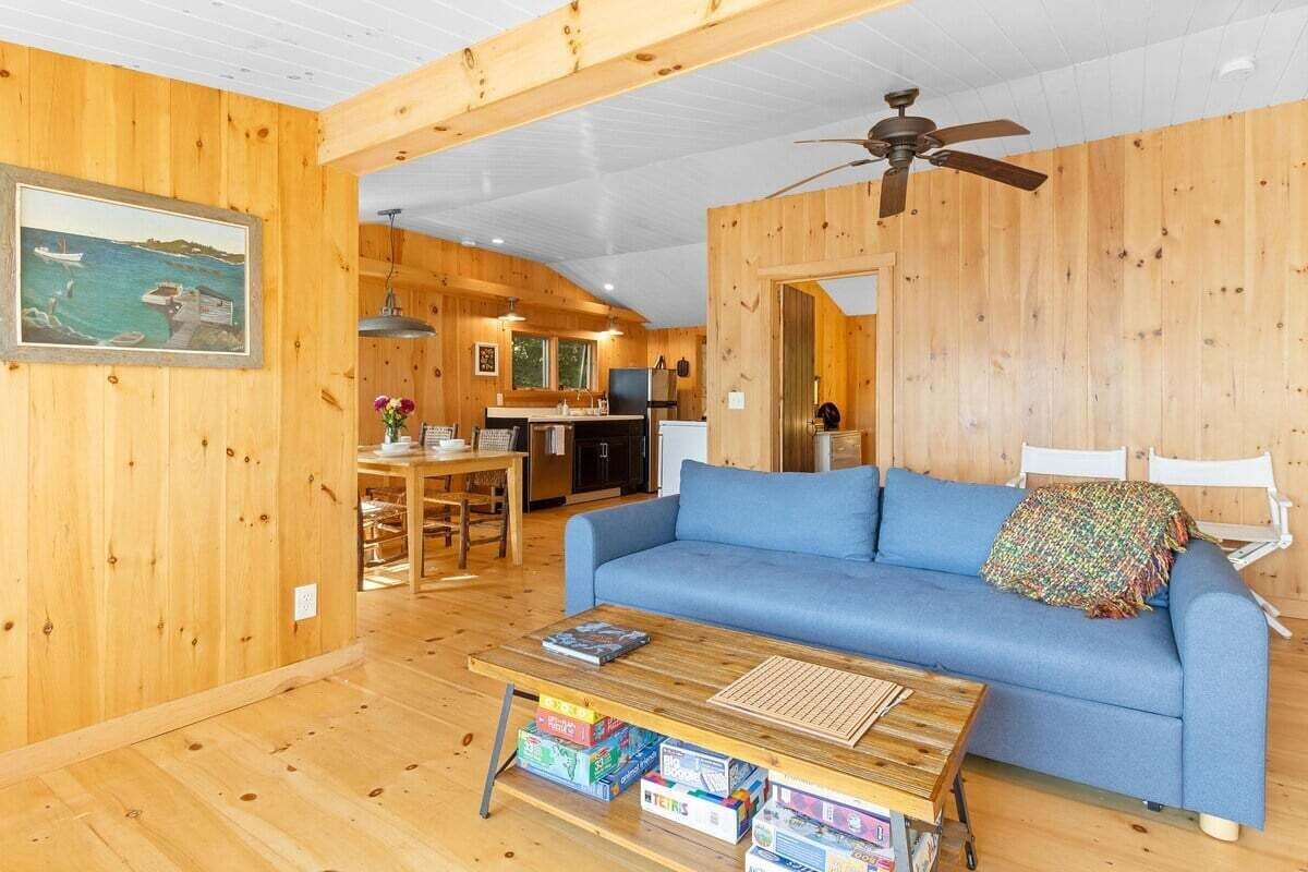 A wooden interior with a sofa, a coffee table with books, a ceiling fan, and a painting on the wall.
