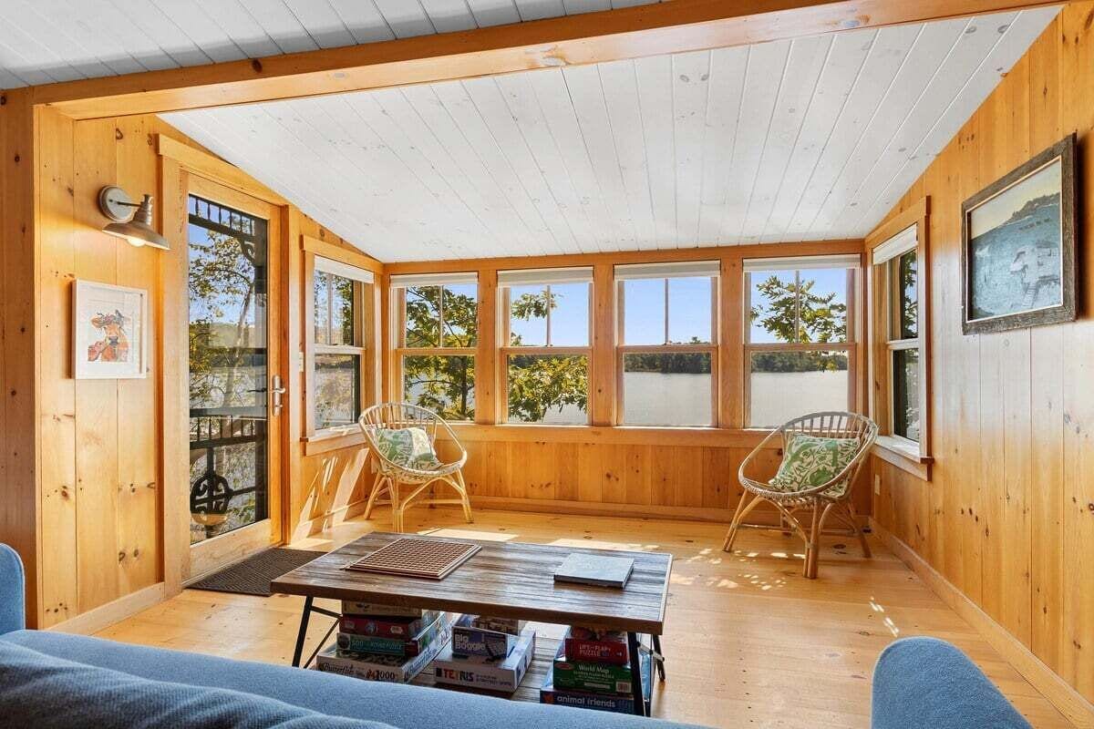 A cozy cabin with wooden walls, large windows, a wooden table, and two wicker chairs.