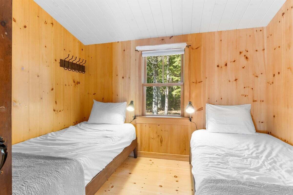 Une cabane avec deux lits, une fenêtre donnant sur la forêt et un mur en bois muni d’un porte-manteau.