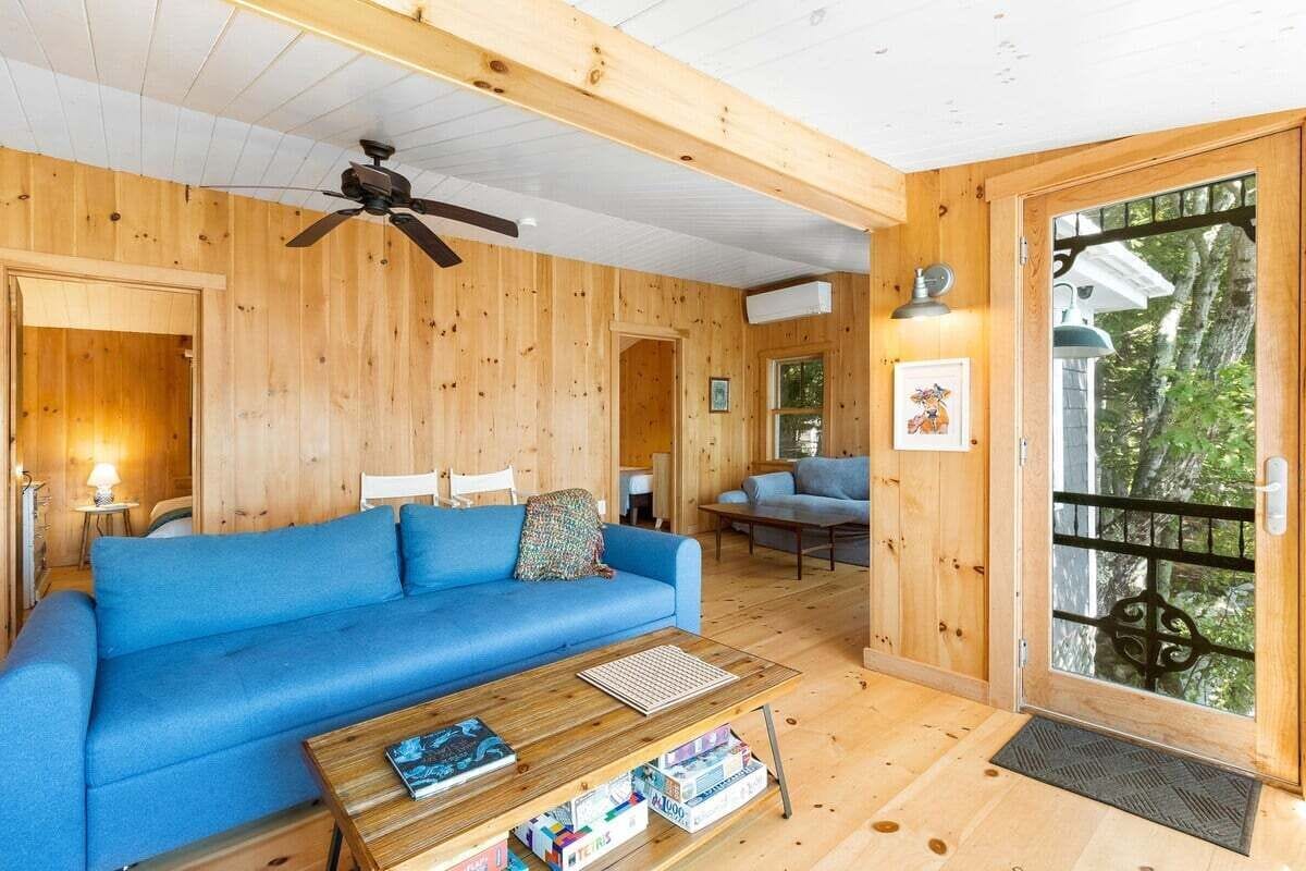 Ein Holzinnenraum mit einem blauen Sofa, einem Deckenventilator und einer zur Außenseite führenden Tür.
