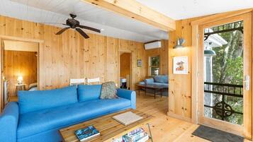 Ein Holzinnenraum mit einem blauen Sofa, einem Deckenventilator und einer zur Außenseite führenden Tür.