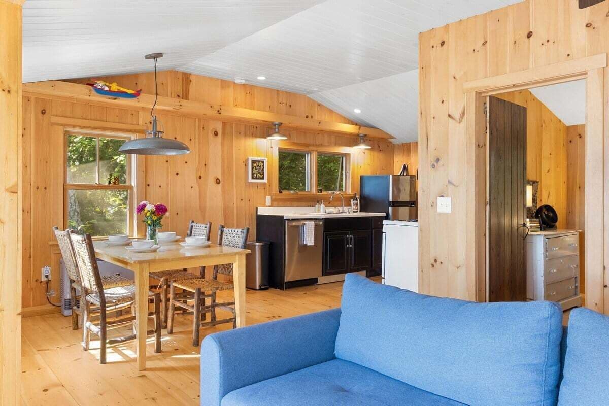 A wooden cabin interior with a dining area, kitchen, and a blue sofa.