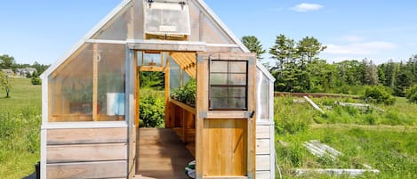 A small, single-story wooden structure with a sloped roof, a door, and a window, situated in a grassy field.