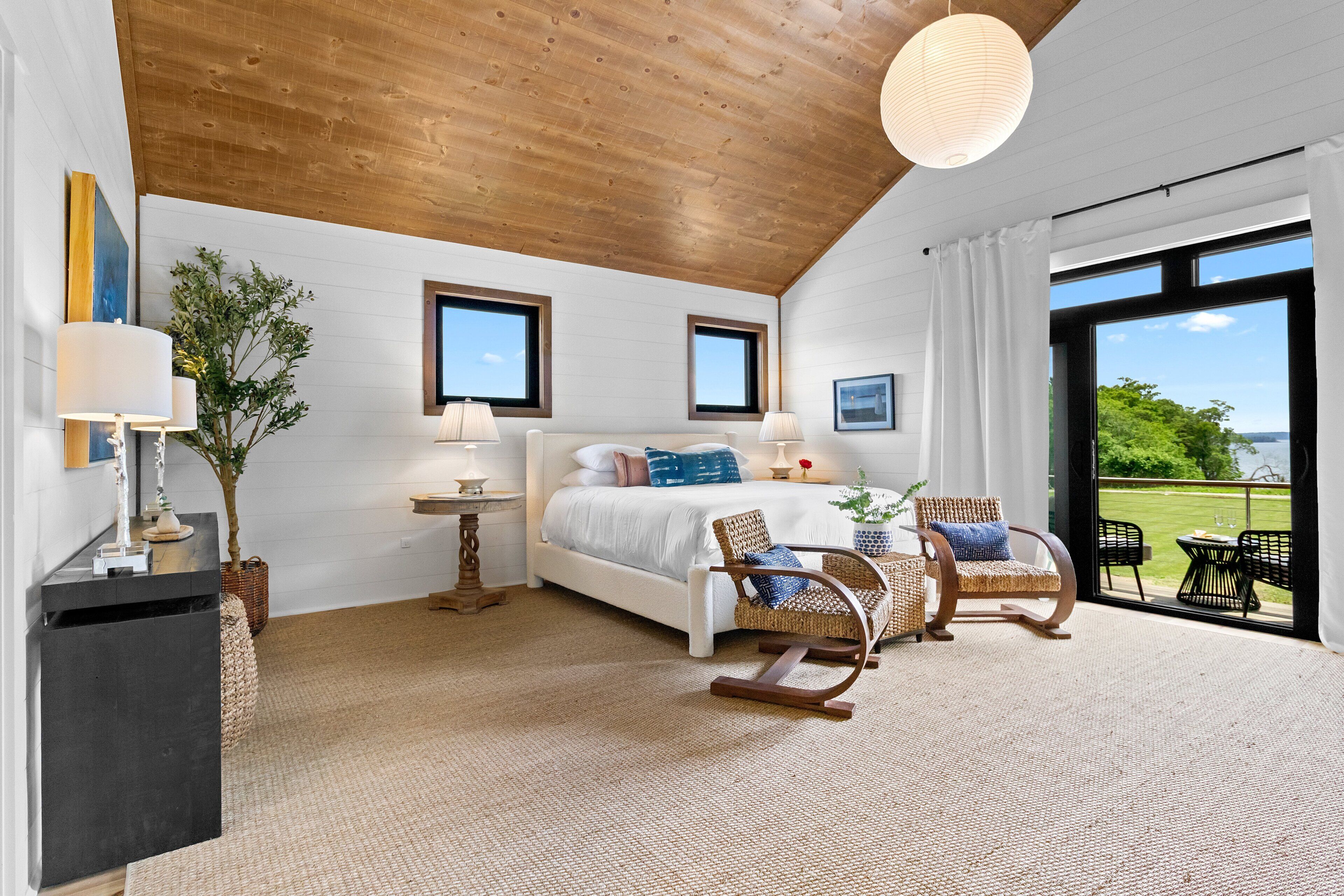 Ein Schlafzimmer mit einem großen Bett, zwei Stühlen, einem kleinen Tisch und Blick ins Freie.