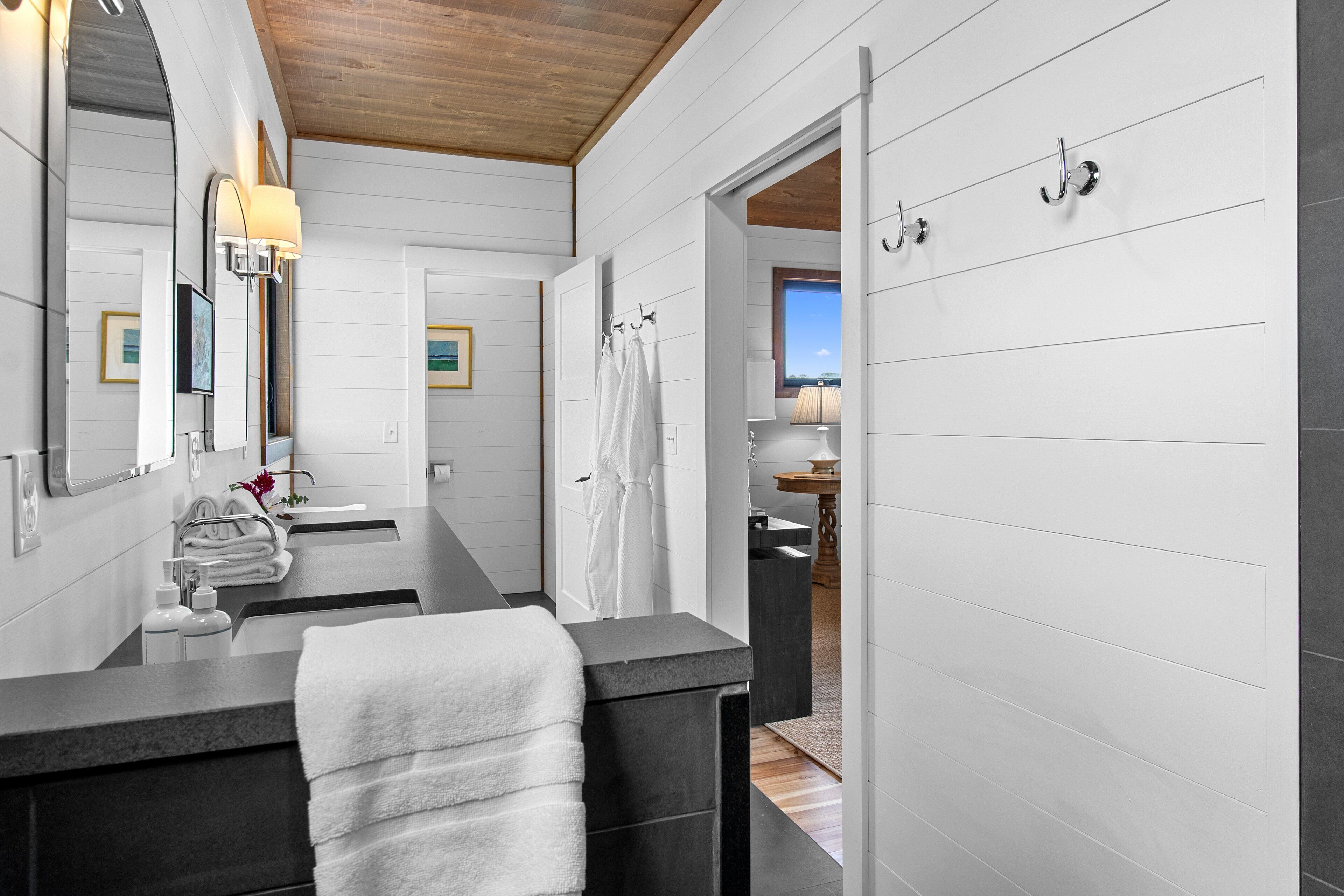 A modern bathroom with a large mirror, two sinks, and a wooden ceiling.