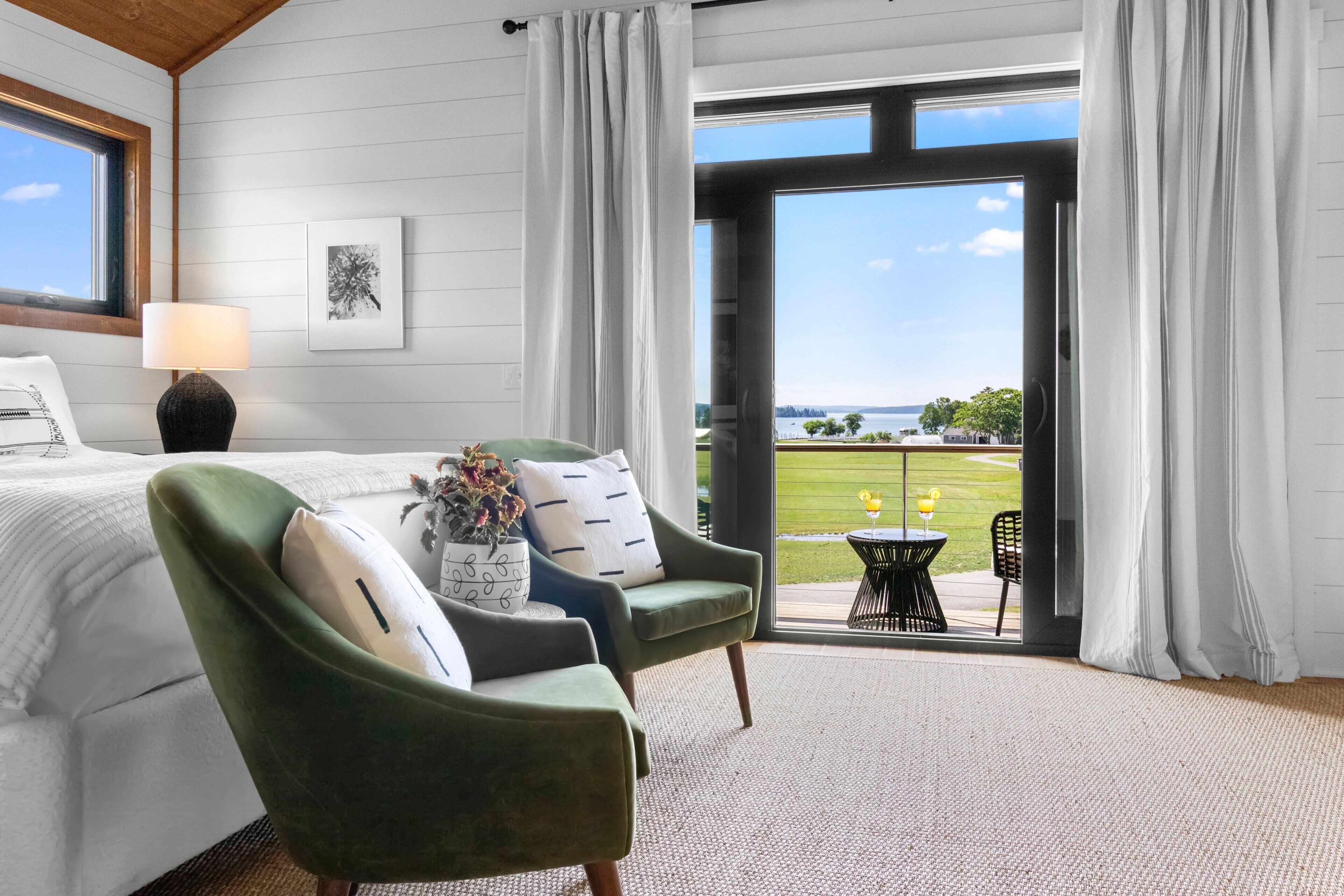 A bedroom with a bed, a chair, a table with a drink, and a view of the outdoors.