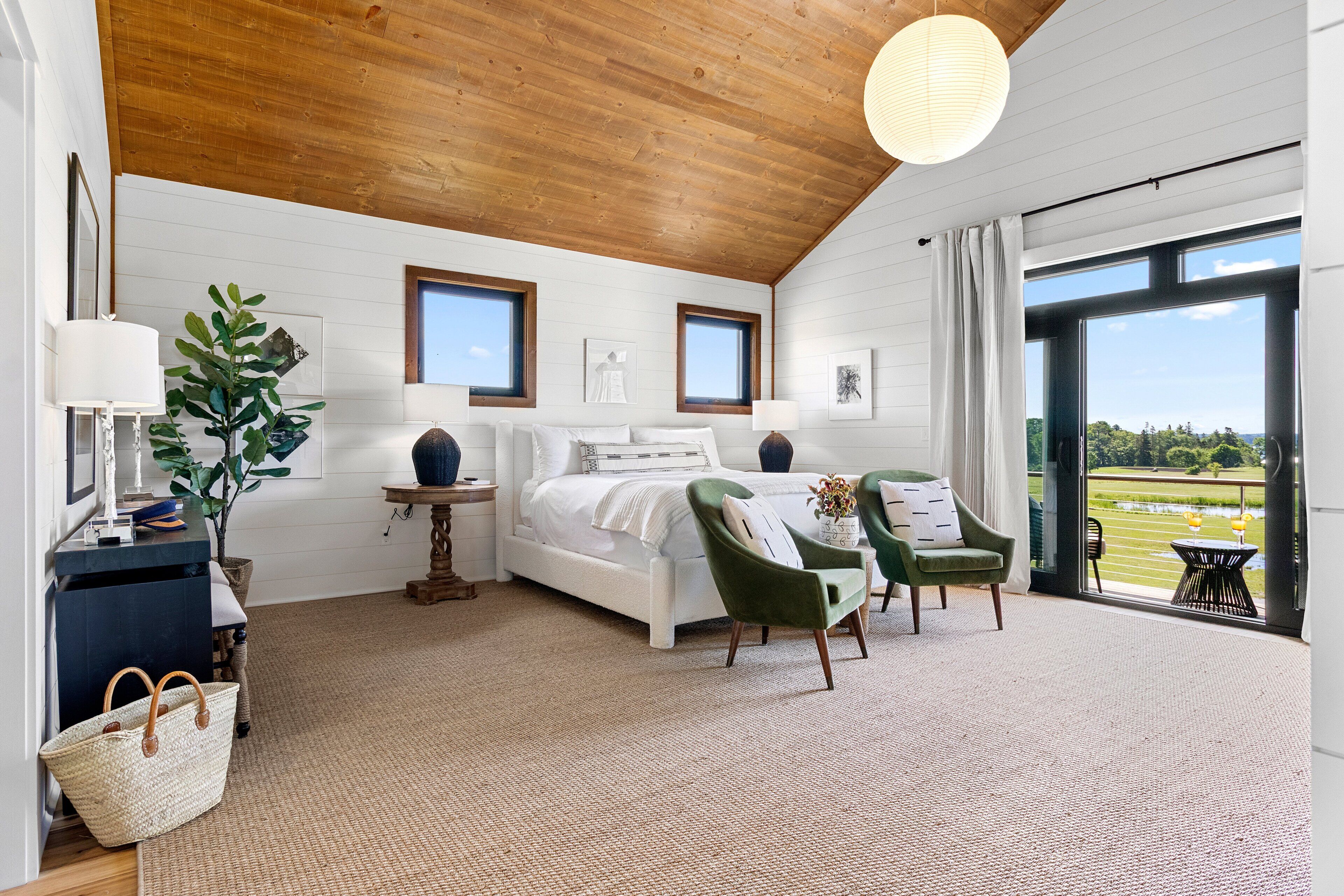 A bedroom with a bed, two chairs, a table, a lamp, and a view of the outdoors.