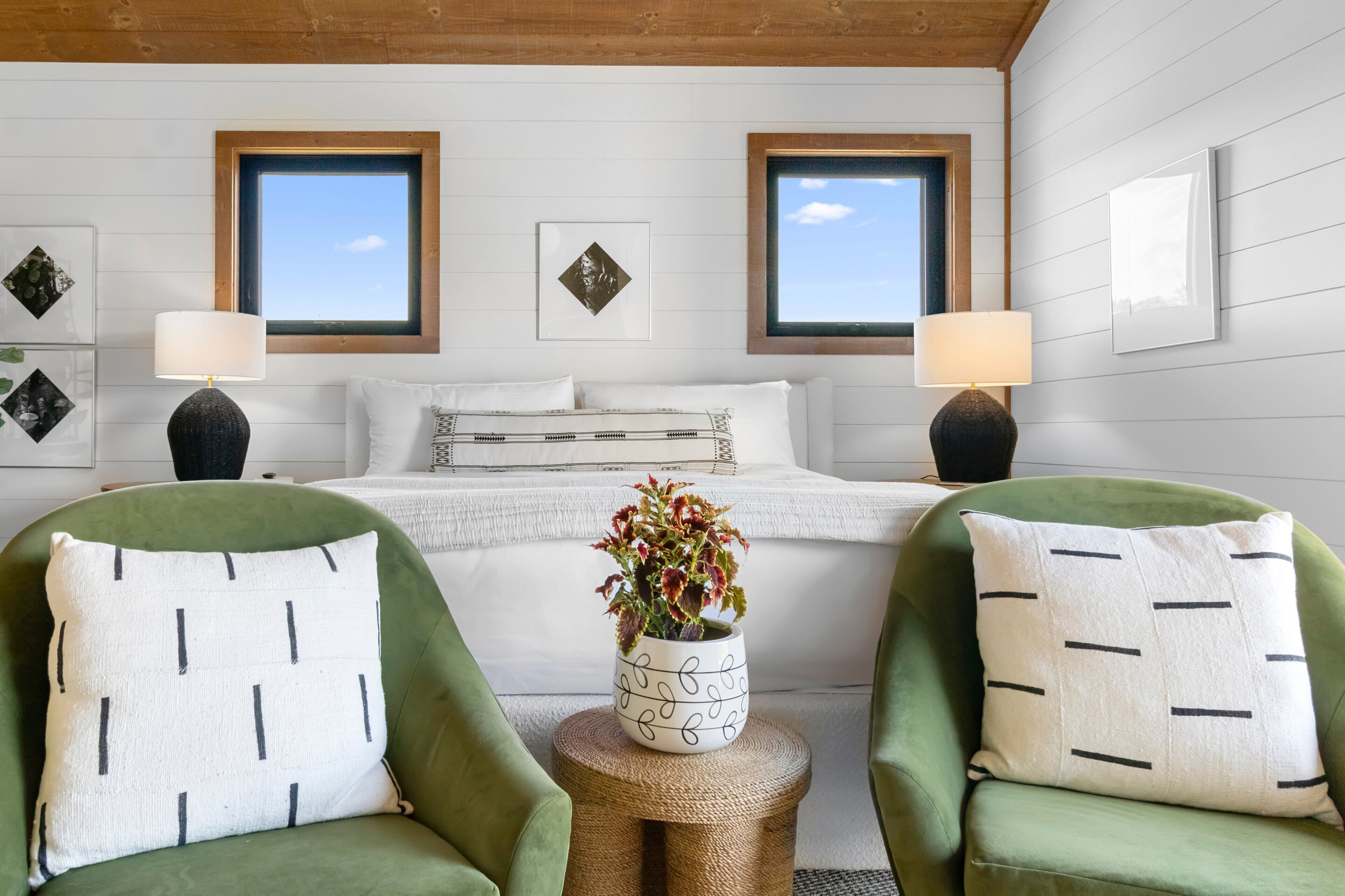 A bedroom with a bed, two chairs, a small table, and two windows.