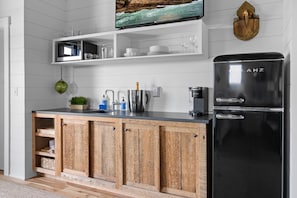 A modern kitchen with a black Galanz refrigerator, wooden cabinets, a black countertop, and a mounted television above the cabinets. - Maggie May, Salt Farm, Romantic & Rural, Perfect for two Near Acadia/bar Harbor (Sullivan)