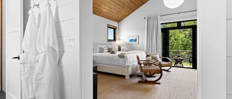 A modern bedroom with a bed, a rocking chair, a view of greenery outside, and a large window.
