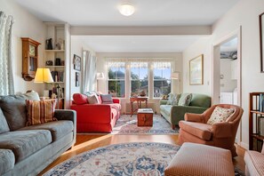 A cozy living room with a red sofa, a grey couch, and a green armchair. There is a wooden coffee table and a patterned rug. - One Atlantic 5BR Harbor View Maine Home, Close to Town, Deck (Boothbay Harbor)