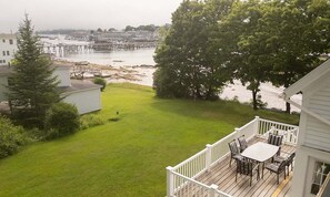 Eine Terrasse mit Gartenmöbeln, die auf einen Rasen und einen Blick auf das Wasser blickt.