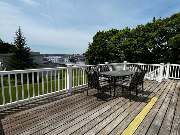 Eine Holzterrasse mit Tisch und Stühlen, mit Blick auf ein Gewässer und einen Steg.