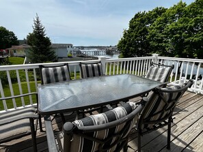 A deck with a glass-top table and striped cushioned chairs, overlooking a body of water and a dock. - One Atlantic 5BR Harbor View Maine Home, Close to Town, Deck (Boothbay Harbor)