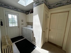 A laundry room with a washer and dryer, a radiator, a black rug, and a door with a window. - One Atlantic 5BR Harbor View Maine Home, Close to Town, Deck (Boothbay Harbor)