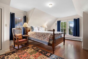 A bedroom with a wooden bed, a rocking chair, a patterned rug, and a view of the outdoors through a large window. - One Atlantic 5BR Harbor View Maine Home, Close to Town, Deck (Boothbay Harbor)
