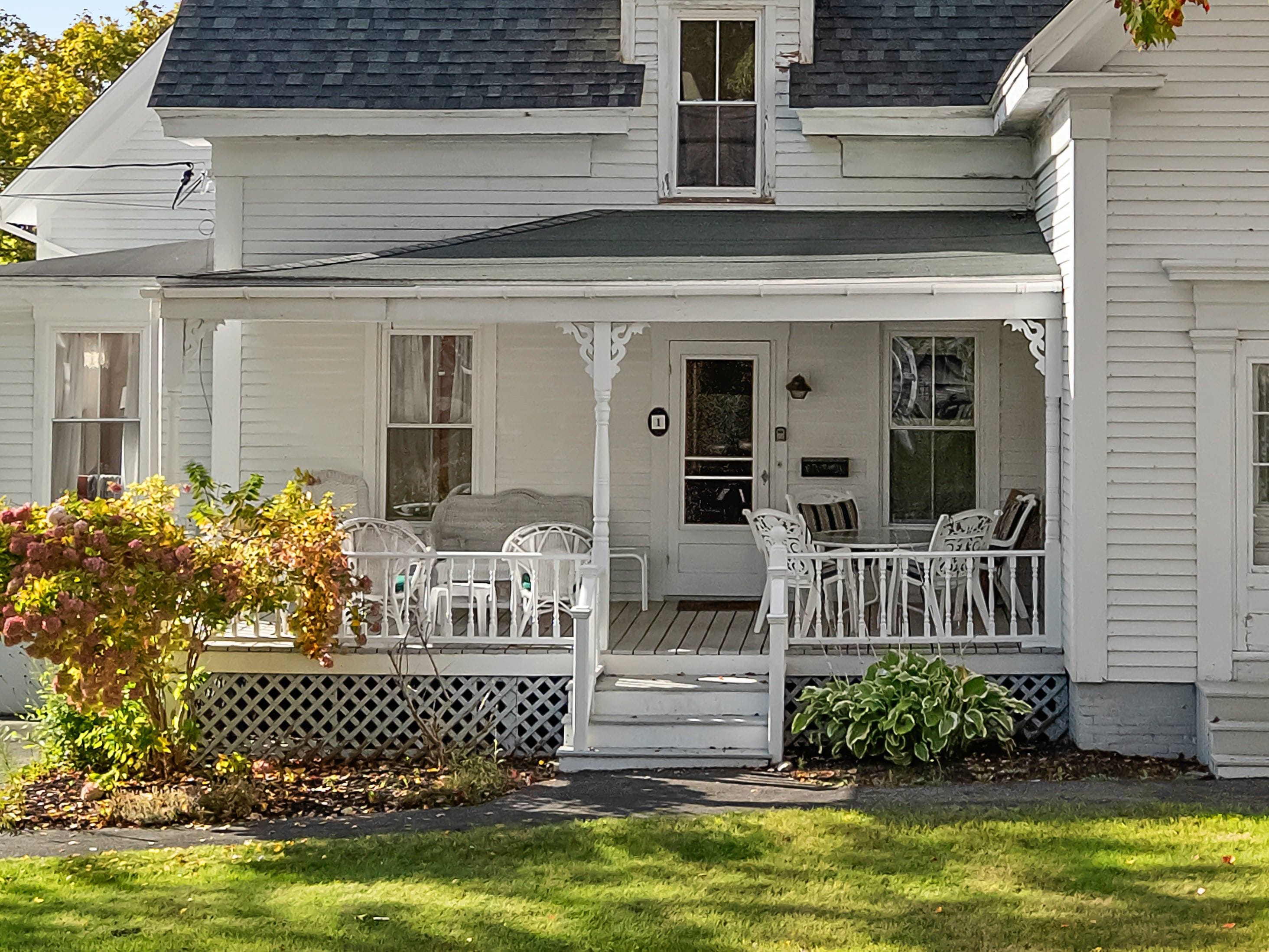 A white house with a porch, a front door, and a small garden.