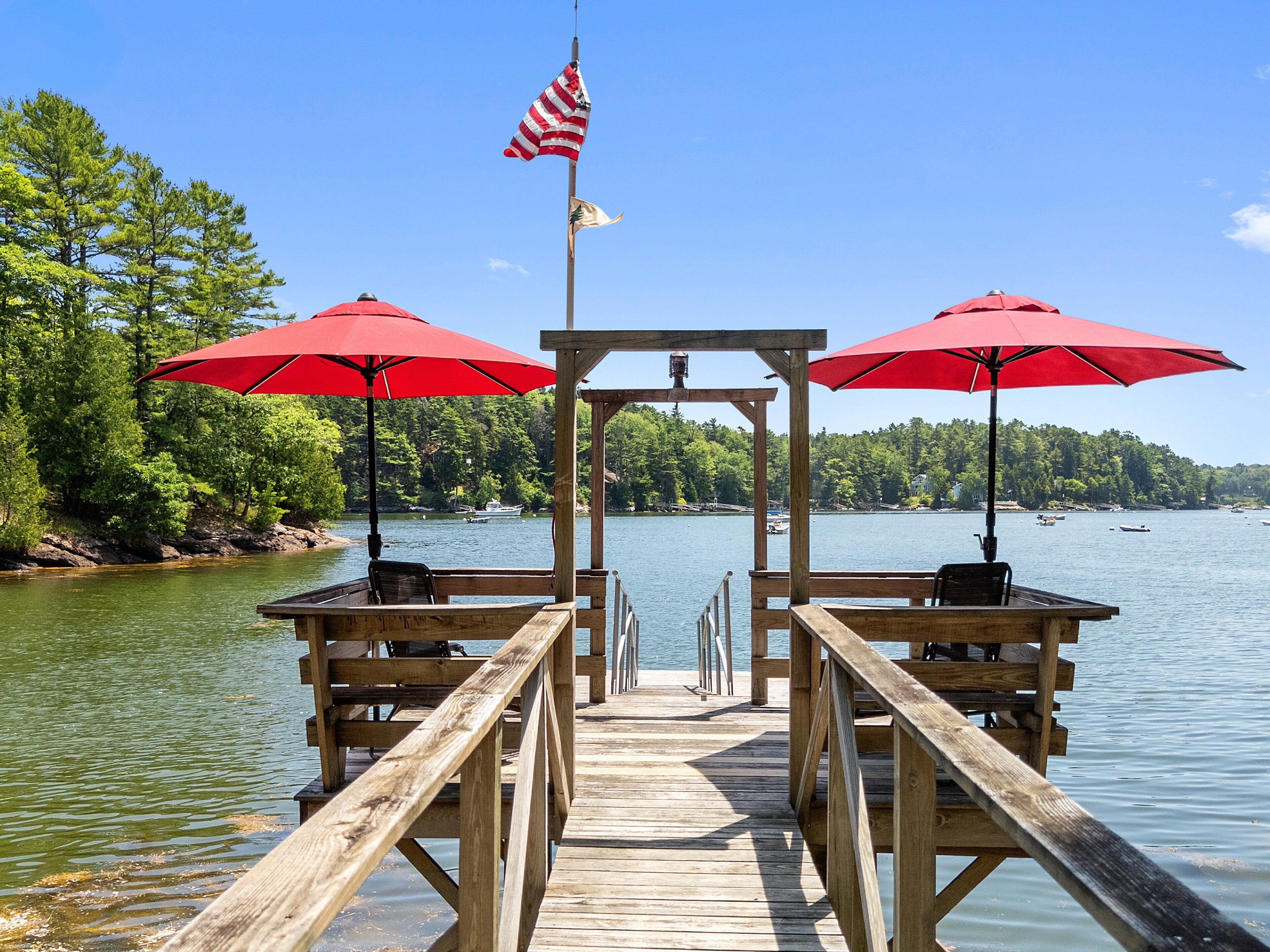 A wooden pier with red umbrellas, a flag, and a view of the lake.