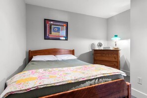 A bedroom with a bed, a dresser, a nightstand, a lamp, and a framed picture on the wall. - The Boathouse (Bath)