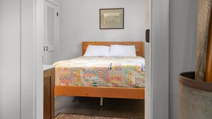 A bedroom with a wooden bed, white pillows, a quilt, a framed picture on the wall, and a wooden floor. - The Boathouse (Bath)