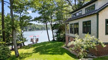 A lakeside property with a dock, grassy lawn, and a house with a brick foundation and white siding.