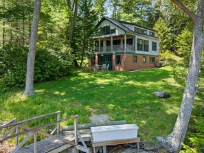 A two-story house with a porch, surrounded by a forested area. - The Boathouse (Bath)
