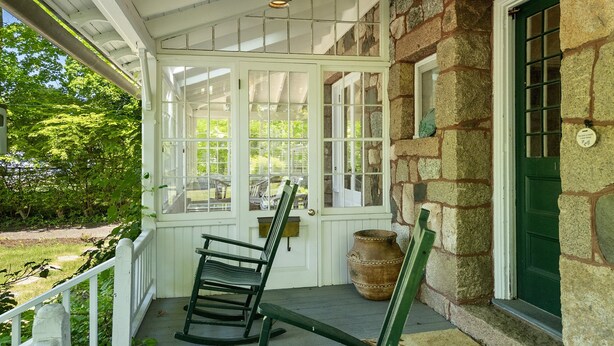 A porch with a rocking chair, a wooden bench, a lantern, and a stone wall with a green door. - La Maisonette - Historic Renovated 6 BR Downtown Bar Harbor (Bar Harbor)