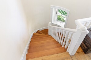 Un escalier en bois avec des rampes blanches et une fenêtre donnant sur un paysage verdoyant.