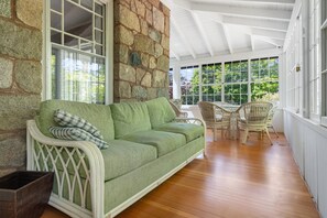 Ein Zimmer mit einer Steinsäule, einem grünen Sofa, Korbstühlen und Holzboden.