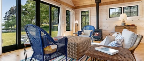 A cozy cabin interior with a large window, a fireplace, wicker furniture, and a striped rug.
