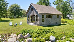 A small, single-story house with a sloped roof, a front porch, and a lawn with outdoor furniture. - Aril Cottage-waterfront Escape With Ocean Views (Prospect Harbor)