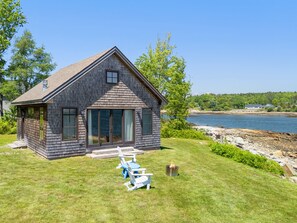 A house with a large window, a deck, and a view of a body of water. - Aril Cottage-waterfront Escape With Ocean Views (Prospect Harbor)