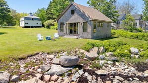 A single-story house with a sloped roof, a front porch, and a large window. - Aril Cottage-waterfront Escape With Ocean Views (Prospect Harbor)