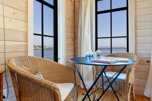 A room with two wicker chairs, a small round table, and a view of the sea through large windows. - Aril Cottage-waterfront Escape With Ocean Views (Prospect Harbor)