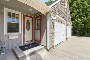 A residential house with a front porch, a red door, and a garage door. - 4-bedroom house in lovely Narragansett with cool ocean breeze (Narragansett)