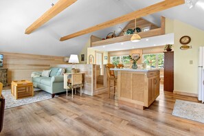 Ein großzügiges Loft mit hohen Decken, Holzbalken, einer Küchenzeile mit Kochinsel, einer Essecke mit Sofa und Stühlen sowie einem großen Fenster für natürliches Licht.