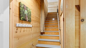 A wooden staircase with a metal handrail and a wall-mounted coat rack with hooks. - Riverbend Perch - River-view Retreat for 2 With Kitchen, Patio, AC, Wi-fi (Cushing)