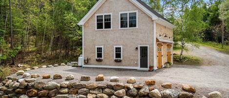 Une maison à deux étages, avec un mur de pierre à l’avant, entourée d’arbres.