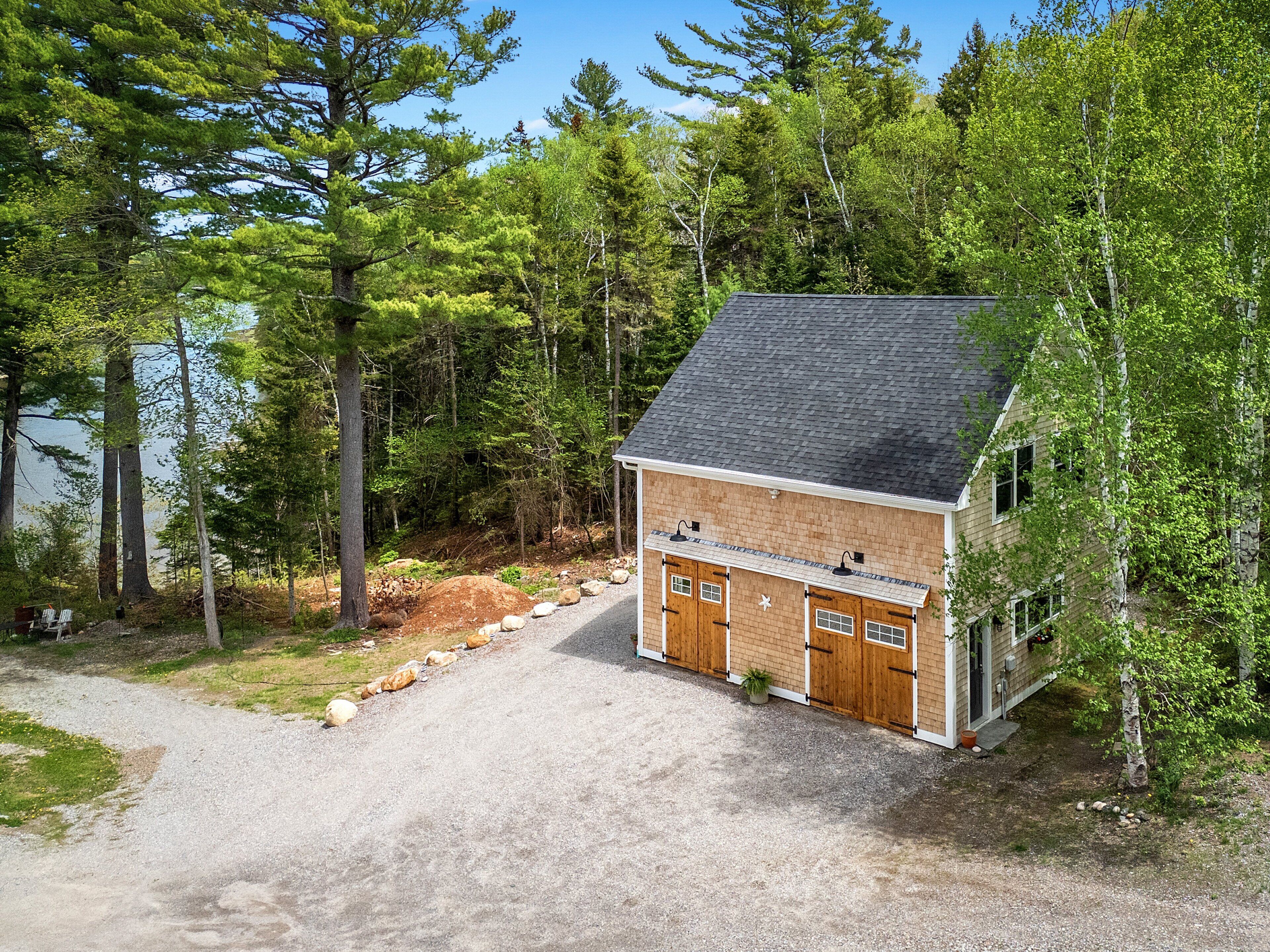 A cabin with a gravel driveway, wooden doors, and a chimney.