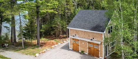 A cabin with a gravel driveway, wooden doors, and a chimney.