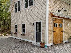 A two-story house with a front door, two windows, and a porch with a potted plant. - Riverbend Perch - River-view Retreat for 2 With Kitchen, Patio, AC, Wi-fi (Cushing)