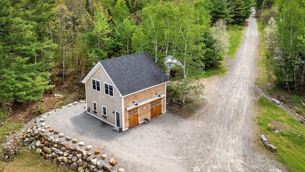 A two-story house with a gravel driveway and a stone wall, surrounded by dense forest. - Riverbend Perch - River-view Retreat for 2 With Kitchen, Patio, AC, Wi-fi (Cushing)