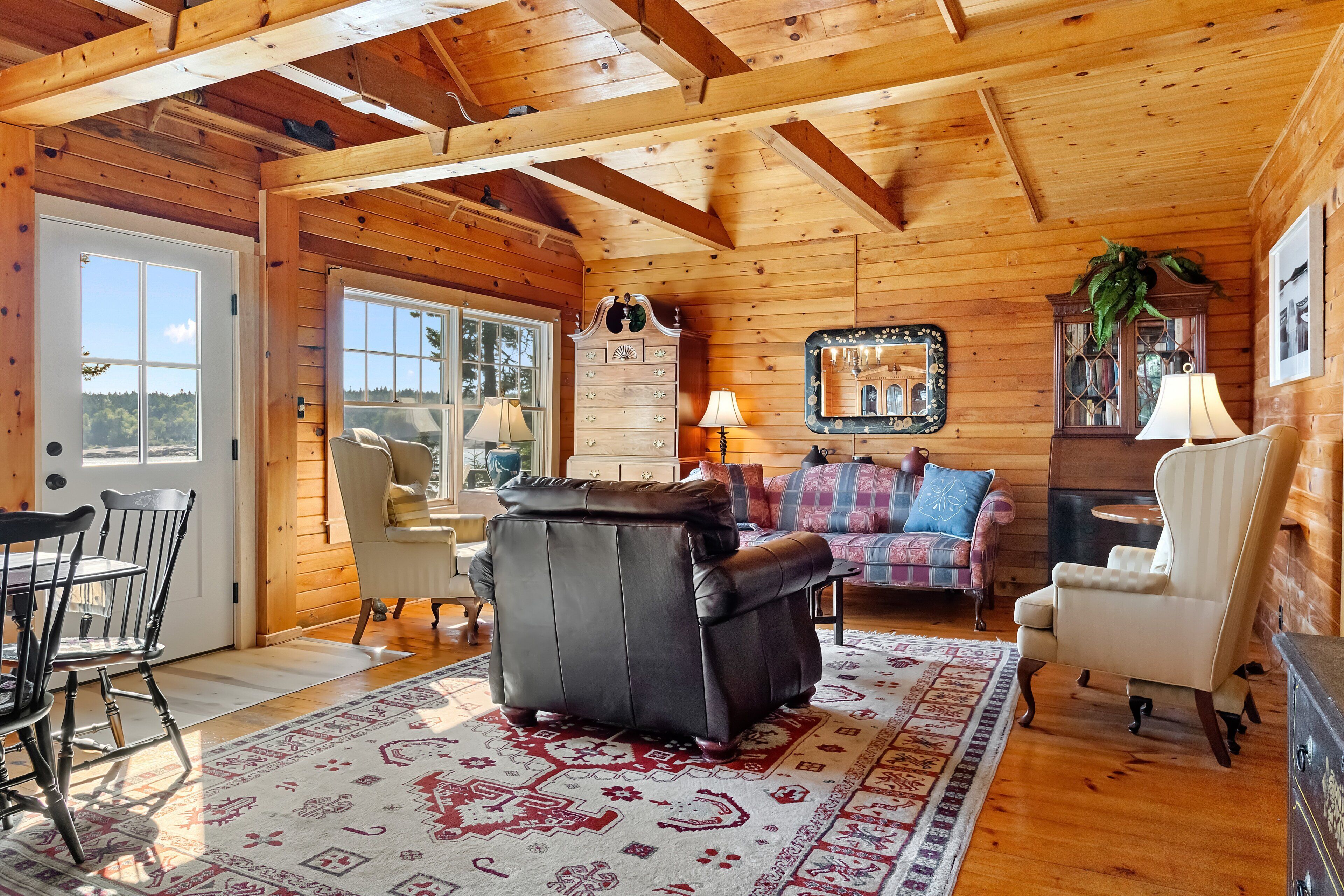 A wooden interior with a sofa, chairs, a table, and a patterned rug.