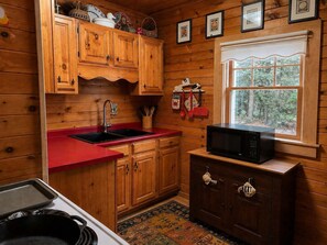 Cocina de cabaña de madera con encimera roja, armarios de madera, microondas y ventana con vistas a árboles.