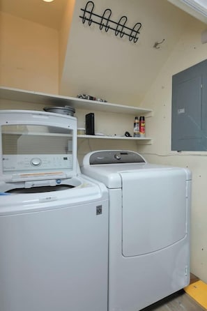 Een wasruimte met een wasmachine en droger, een plank met schoonmaakmiddelen, en een wandrek.