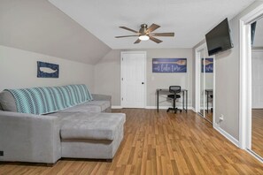 A living room with a grey sofa, a ceiling fan, a flat-screen TV, and a wooden floor. - Lake Days & Cozy Nights | Lake Murray Getaway (Lexington)